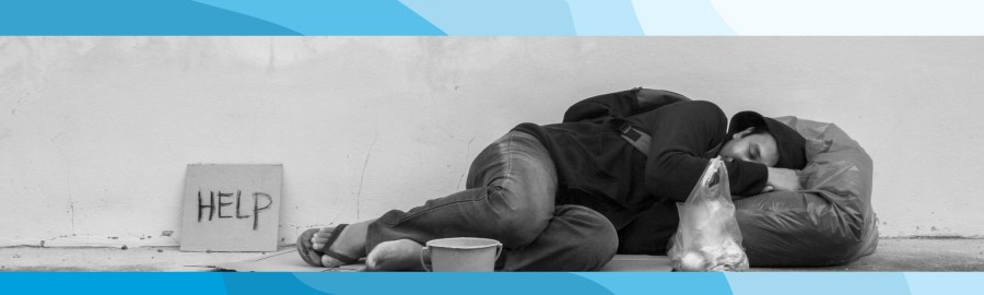 A man in a coat laying on a sidewalk with a sign that says help